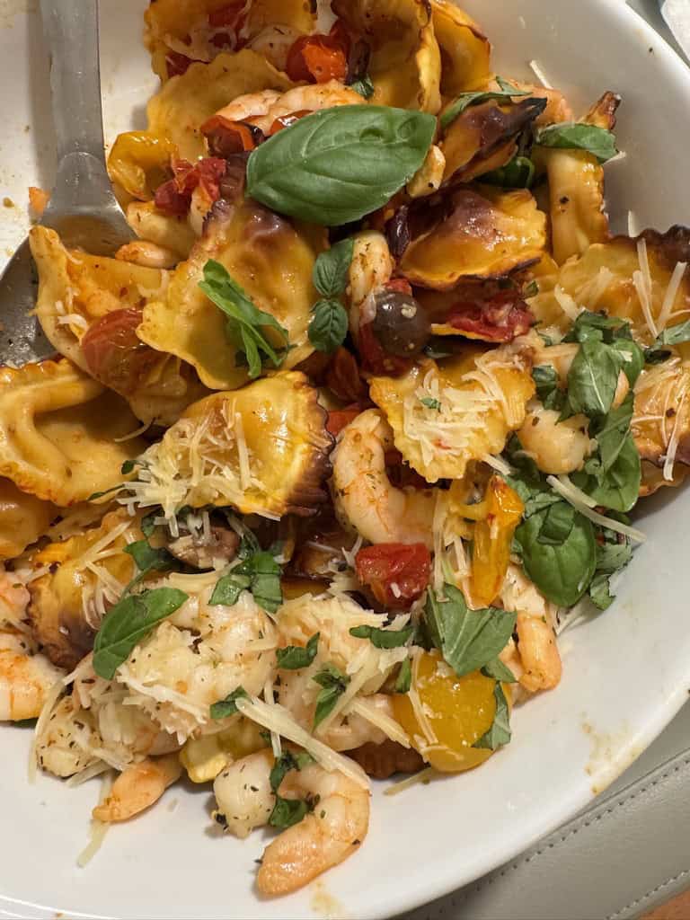 Shrimp pasta with grated cheese, basil leaves, and tomatoes on a white plate.